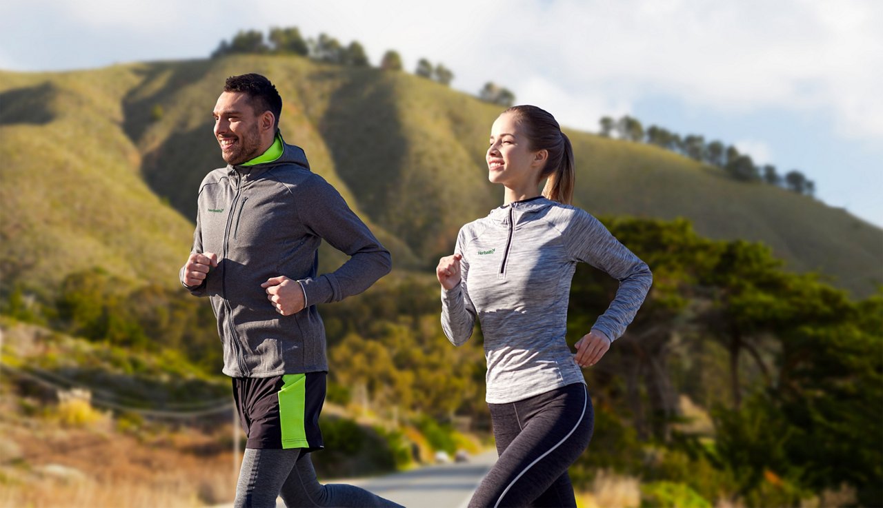 A man and woman running outdoors, wearing Herbalife branded apparel